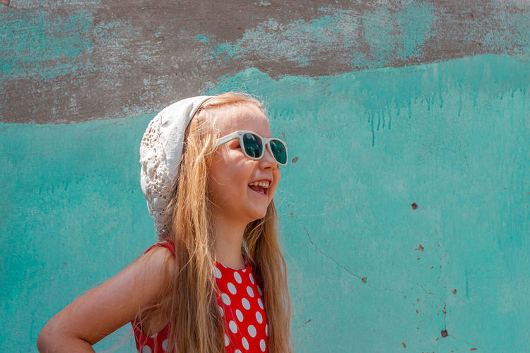 Beautiful happy girl in red polka dot dress smiling turquoise concrete wall background. cute child 