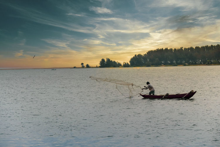 Man fishing in sea while standing on boat at sunset