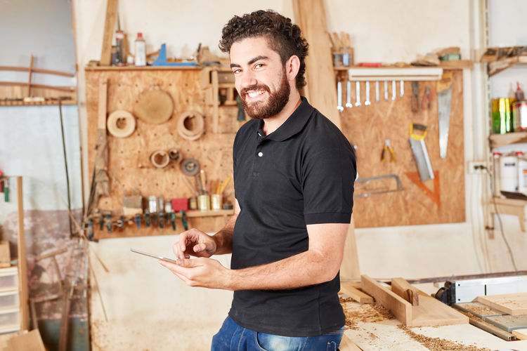 Portrait of smiling carpenter using mobile phone at workshop