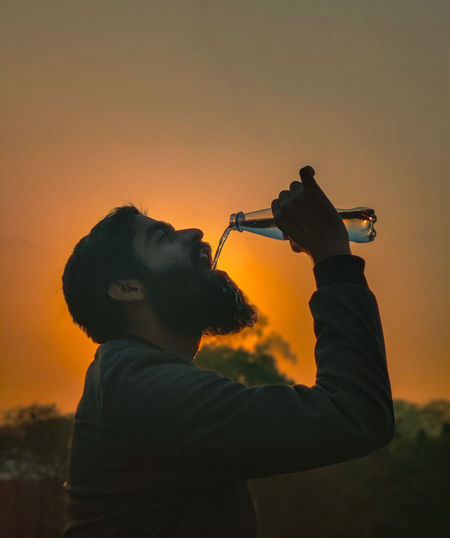 Side view of man photographing against sky during sunset
