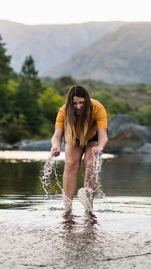 Full length portrait of woman splashing water while standing in lake