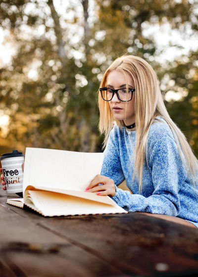 Young woman reading book and enjoying coffee in park
