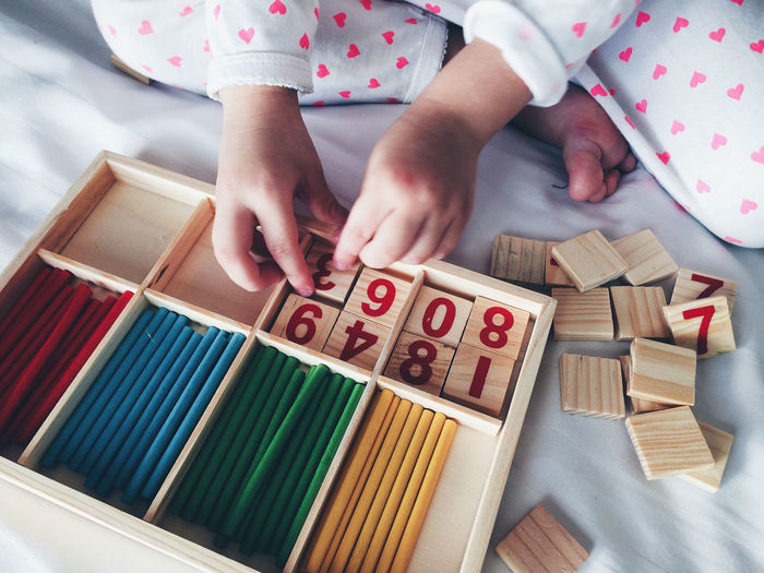 High angle view of child arranging blocks with number in box on bed