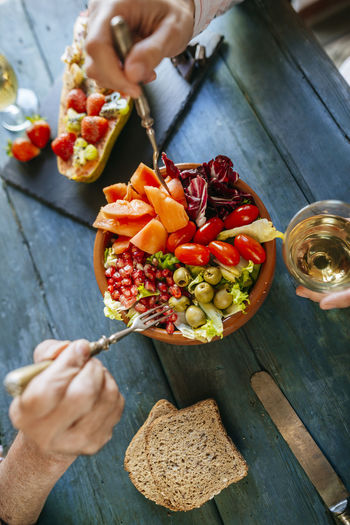 Close-up of woman's hands eating salad of tomato, pomegranate, papaya and olives
