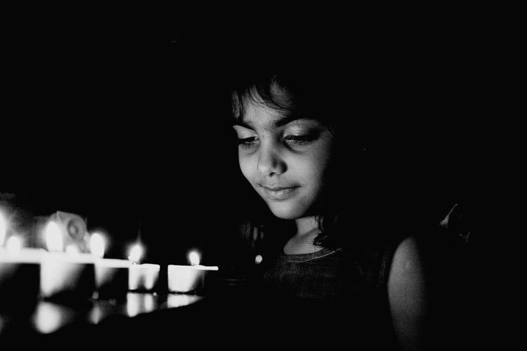 Close-up of cute girl looking at illuminated tea lights at night
