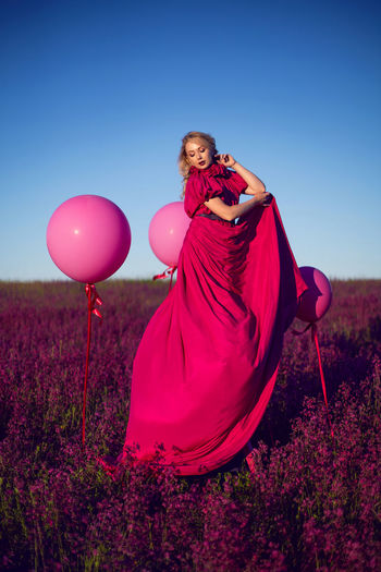 Beautiful young woman on a pink stepladder in a pink dress in a field with wildflowers in summer
