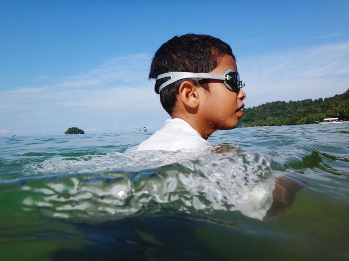 Side view of boy swimming in sea against sky