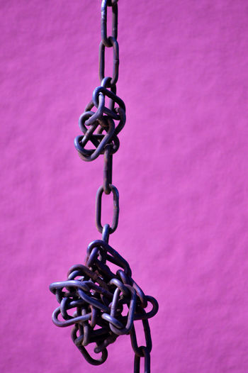 Close-up of metal chain hanging against pink wall