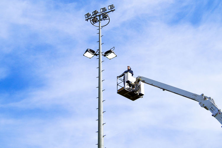 Low angle view of man standing in cherry picker against sky