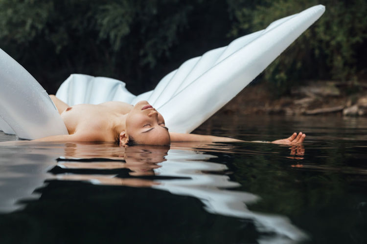 Sensuous naked woman lying over inflatable raft in lake