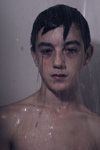 Close-up portrait of teenage boy under shower in bathroom
