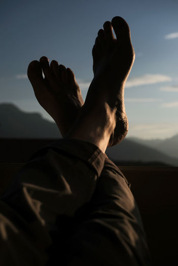 Low section of man with feet up against sky