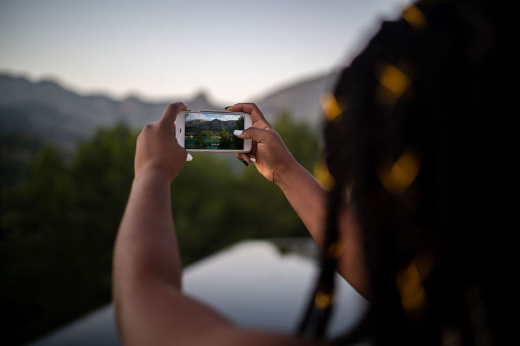 Unrecognizable crop african american female traveler taking picture on smartphone of pond in highlands