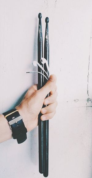 Cropped image of hand holding drumstick against wall