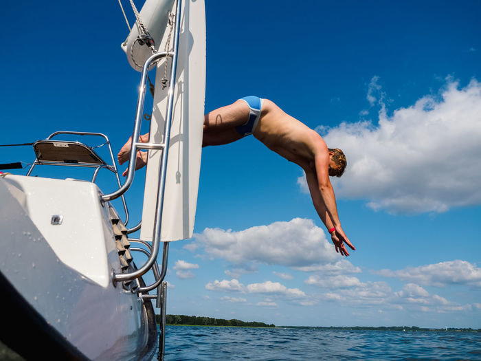 Low angle view of shirtless man jumping in sea against sky