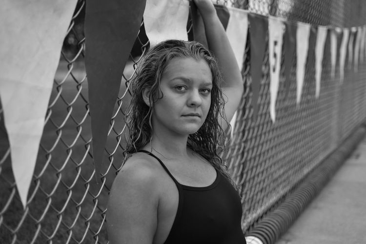 Portrait of young woman in swimwear by chainlink fence
