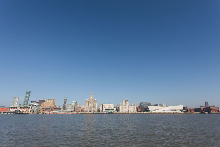 View of cityscape in front of sea against clear sky