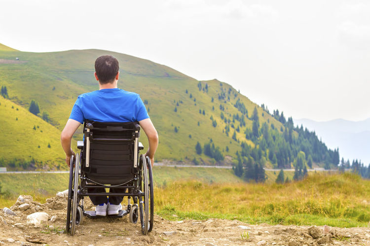 Rear view of man sitting on wheelchair against mountain