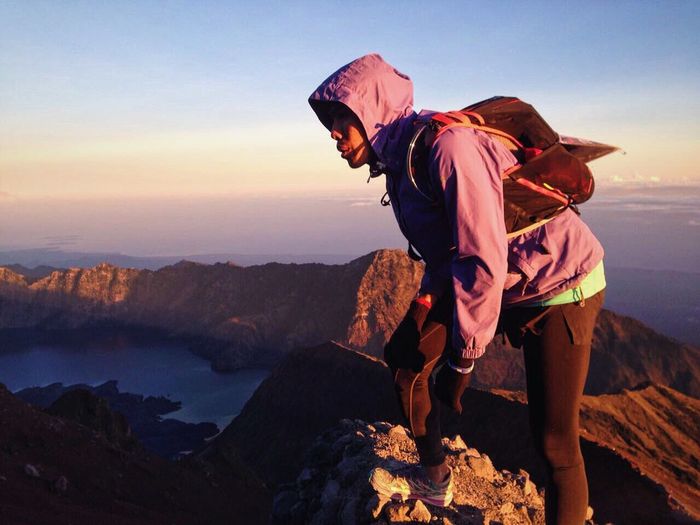 Hiker standing on rock at mount rinjani against sky during sunset