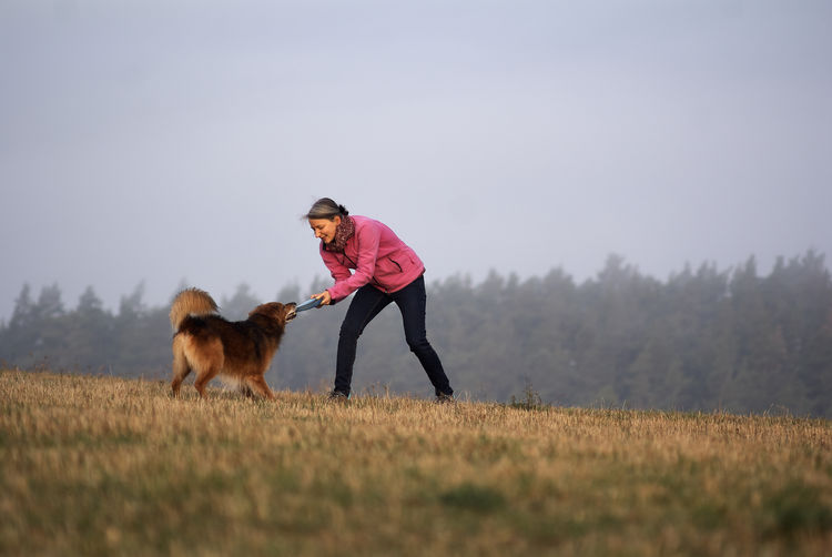 Woman with dog playing on agricultural field