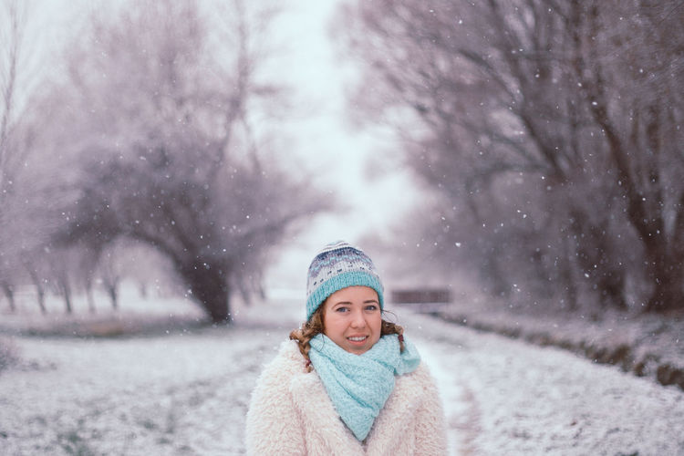 Portrait of young woman standing at park during snowfall