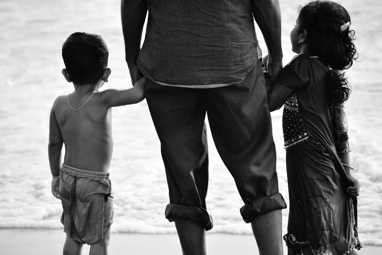 Midsection of father with children standing at beach