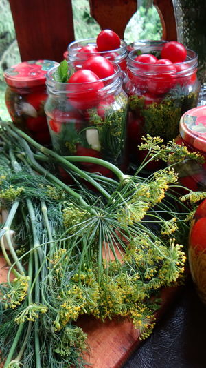 Close-up of tomatoes in glass jars by dill on table