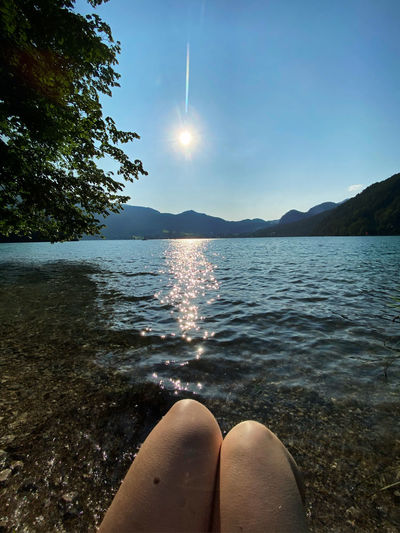Low section of person relaxing in lake against sky