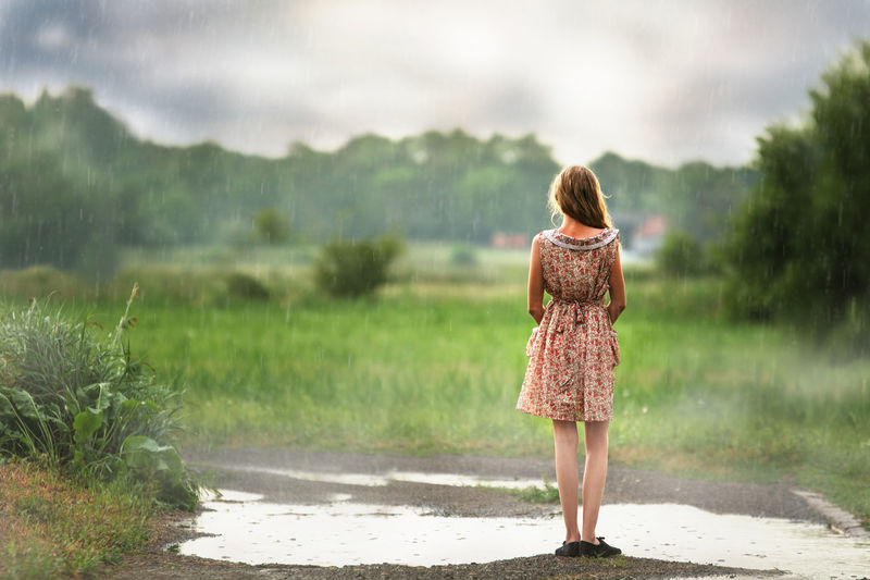 Rear view of woman standing on field against cloudy sky