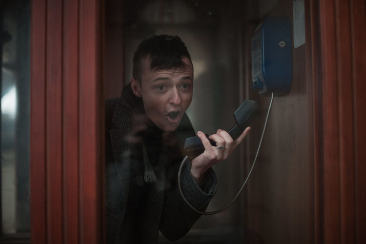 Young man talking on telephone seen through glass