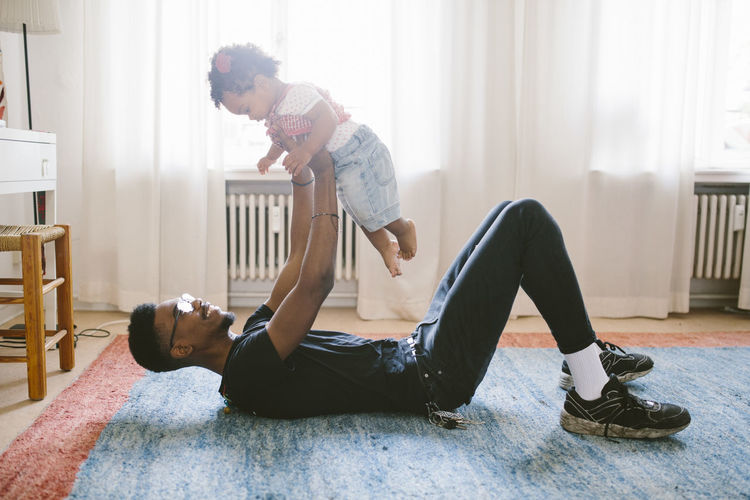 Playful father lifting daughter while lying on carpet at home
