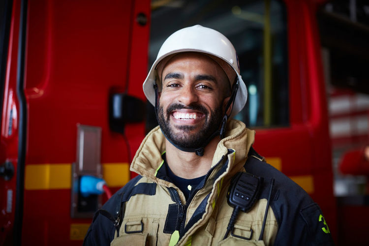 Portrait of smiling firefighter wearing helmet standing at fire station