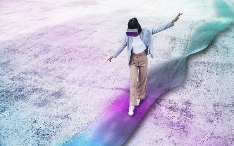 Teenage girl using virtual reality simulator with arms outstretched walking on multi colored wave path