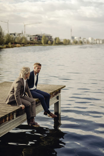 Two businessmen sitting on jetty at a lake