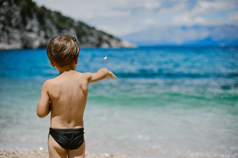 Rear view of shirtless boy standing at beach
