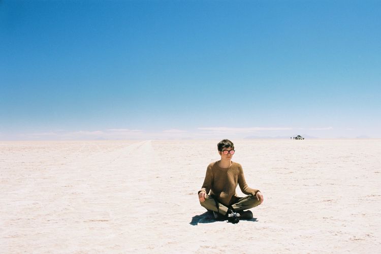 Full length of woman sitting on sand at desert against clear blue sky during sunny day