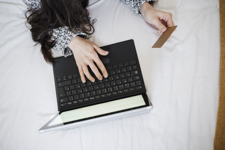 Woman with credit card doing online shopping through laptop on bed