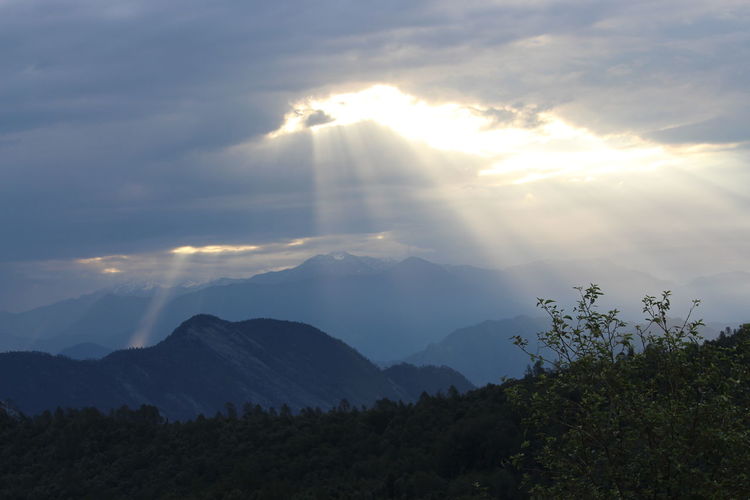Sunlight streaming through mountains against sky
