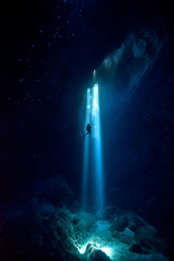 Sunlight falling on silhouette person scuba diving undersea