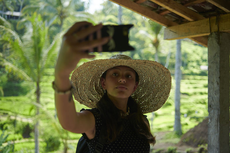 Teen girl wearing a big straw hat taking selfies using mobile phone