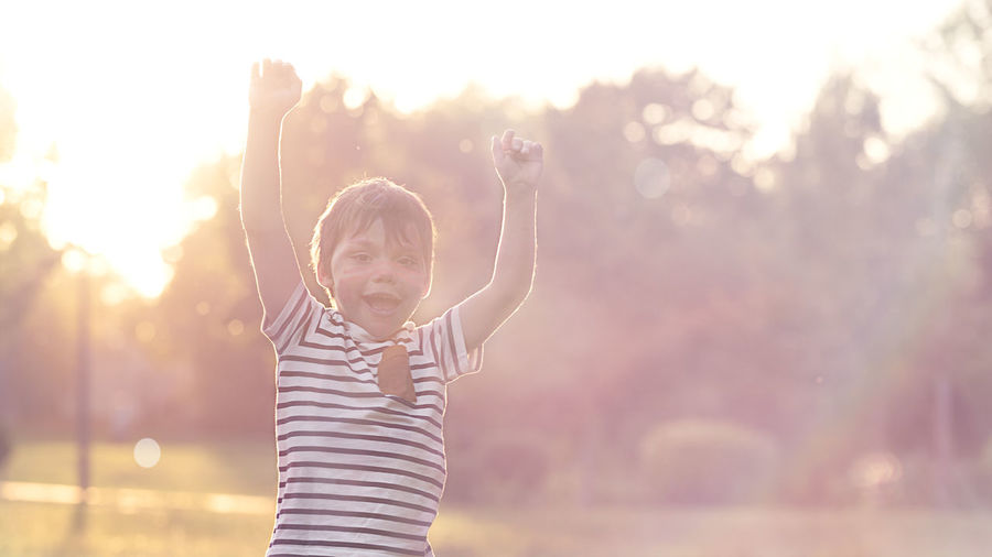 Boy in the sunset light in the park enjoys life raising his hands