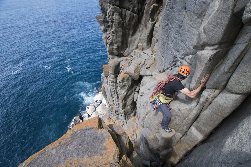Male adventurer heads off into the unkown, armed with ropes and climbing gear, as he explores dolerite rock columns in the sea cliffs of cape raoul, in tasmania, australia.