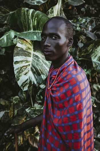 Maasai man in traditional clothes standing in front of green leaves