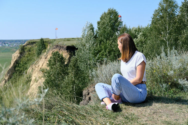 Full length of young woman sitting on land against sky