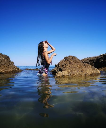 Reflection of woman on rock in water against clear sky