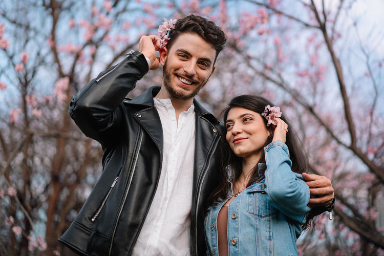 Young couple smiling in front of blooming trees in spring