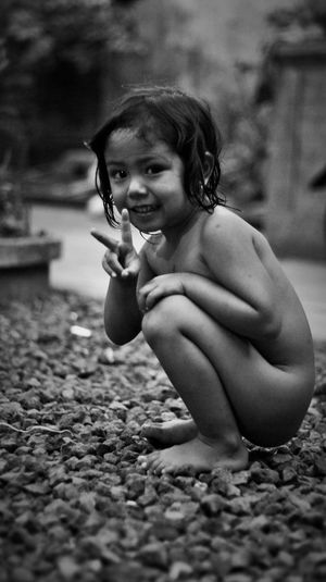 Portrait of smiling naked girl showing peace sign while crouching on rocks