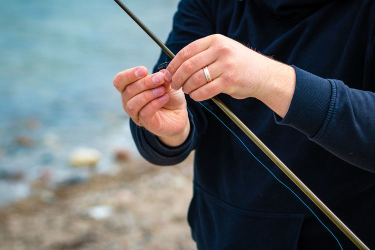 Midsection of man holding fishing rod at beach