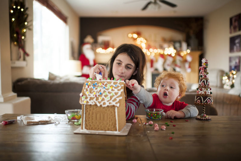 Two kids decorating a gingerbread house for the holidays at home