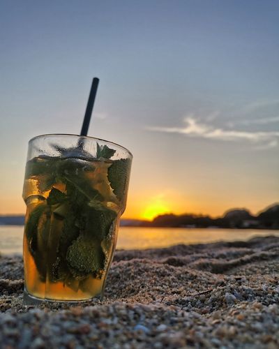 Close-up of drink on table at beach during sunset